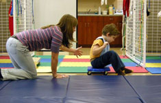 Therapist pushing boy on scooterboard